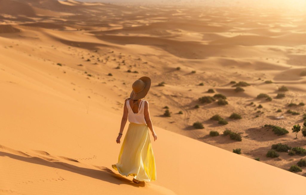 Woman walking on the golden dunes of Merzouga Desert, Morocco